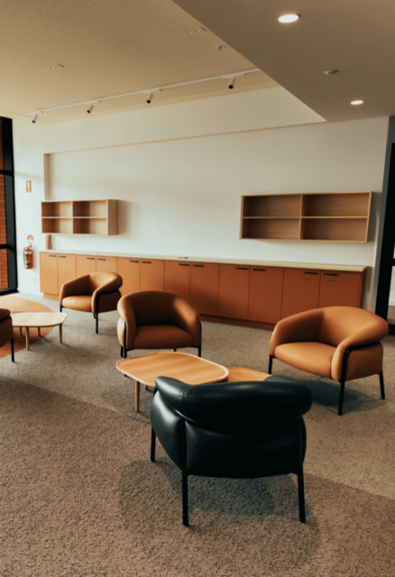 A communal lounge area with chairs, low tables, and built‑in shelving along one wall.