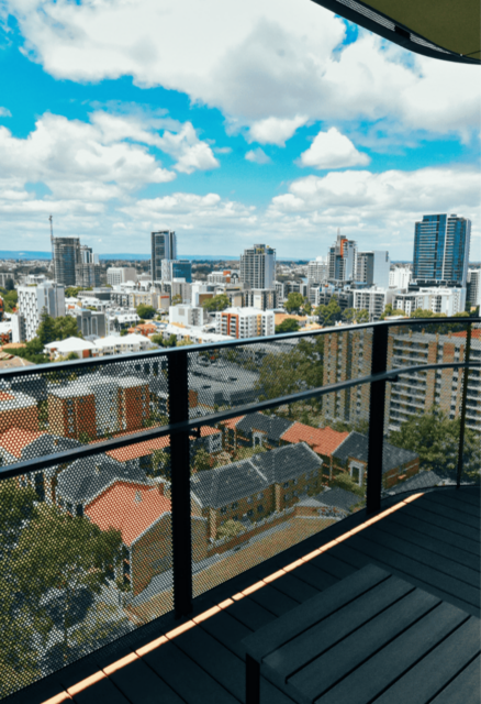 A high‑rise balcony overlooking a cityscape with multiple buildings under a partly cloudy sky.