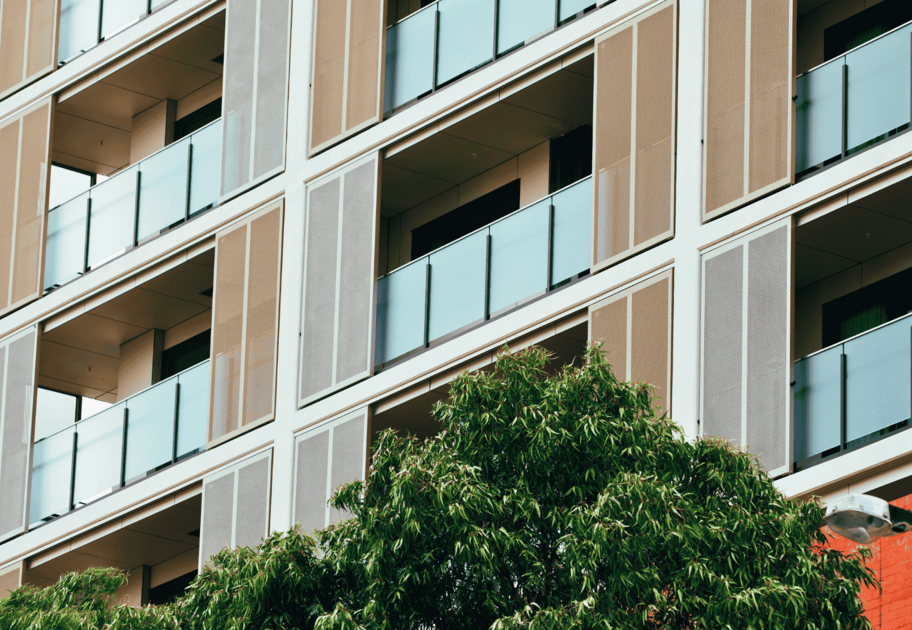 Exterior view of a multi‑storey building with glass‑panel balconies and trees in the foreground.