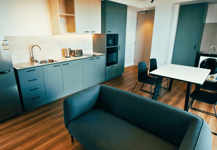 Modern studio kitchen and living area featuring built‑in cabinetry, a sink, appliances, a dining table with chairs, and a sofa.