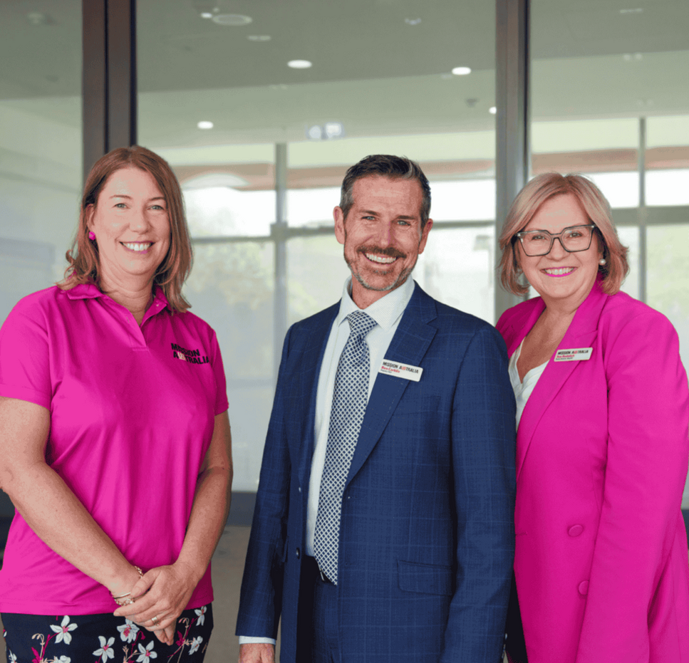 Three Mission Australia leaders stand together indoors, smiling, during an official opening event inside a modern building.