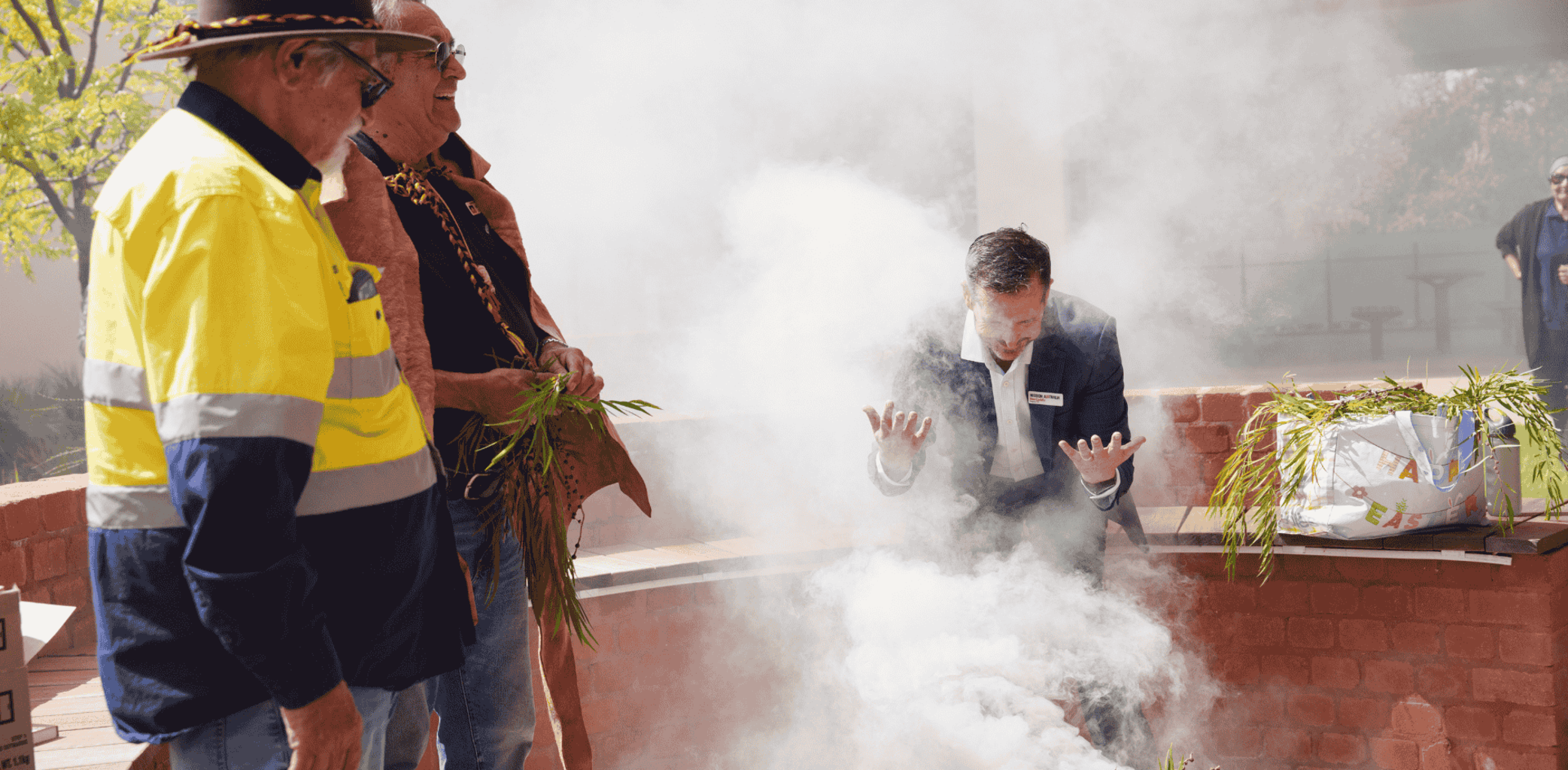 People stand around an outdoor fire as smoke rises during a cultural ceremony in a courtyard setting.