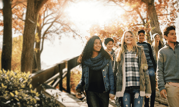 A group of teenagers walk down outdoor steps surrounded by autumn trees with sunlight shining through the leaves.