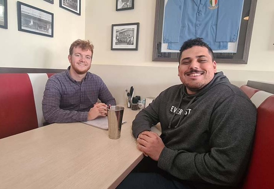 NDIS participant enjoying a milkshake, sitting at table with his NDIS support worker.