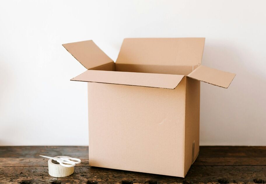 Open cardboard moving box with packing tape and scissors on a wooden table