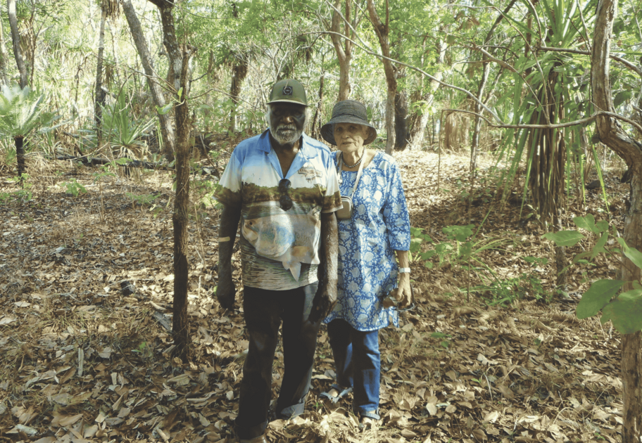 Two people walking through a wooded bushland area surrounded by trees and native plants
