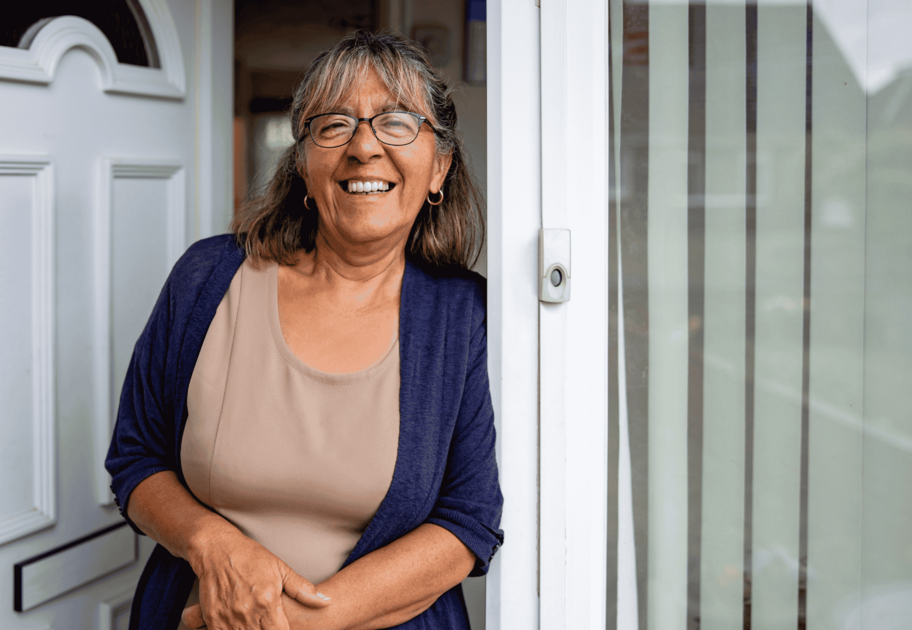 Person wearing glasses standing at the front door of a home beside an open screen door.